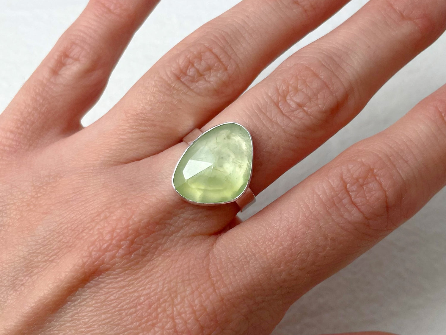 Hand wearing a ring with a green gemstone on a plain background