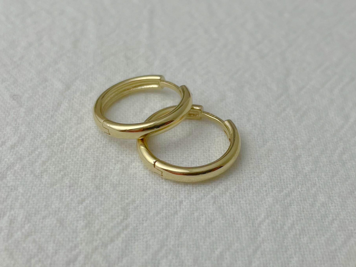 Pair of 14k yellow gold huggie hoop earrings with a polished finish, displayed on soft white fabric
