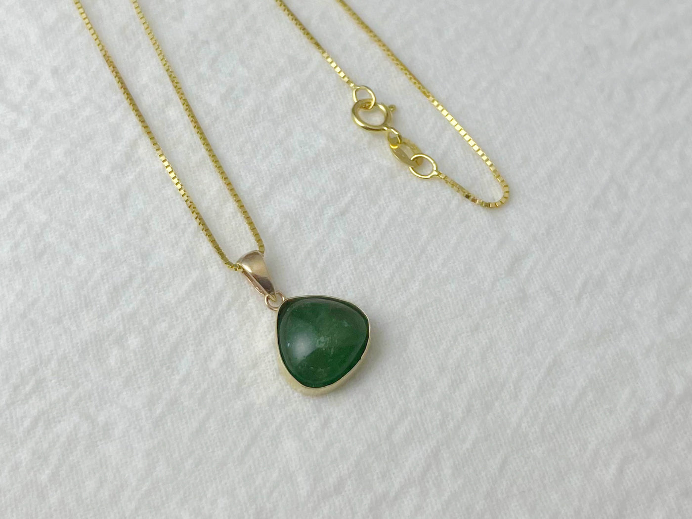 Gold necklace with a green pendant on a white background