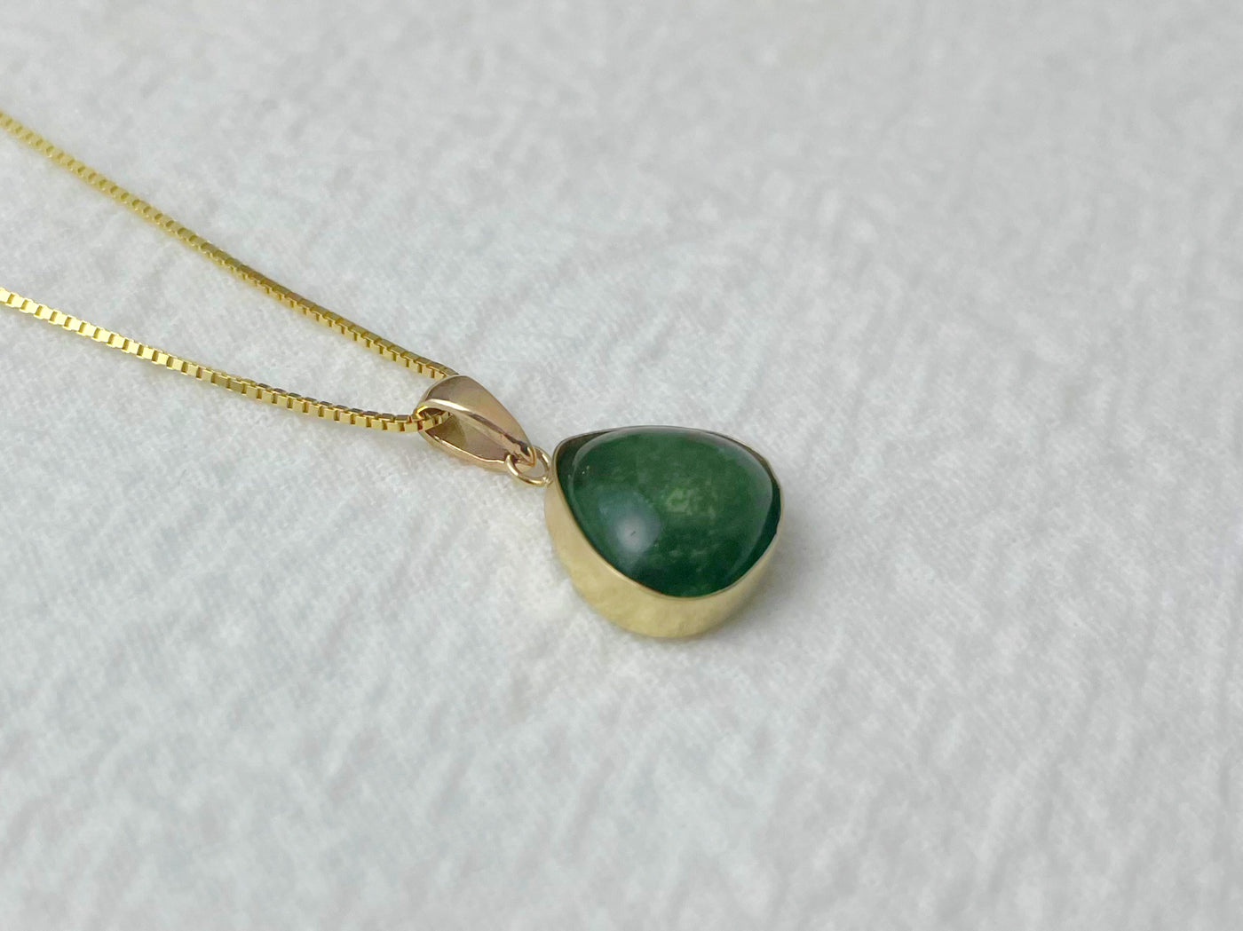 Green teardrop pendant on a gold chain against a light gray background
