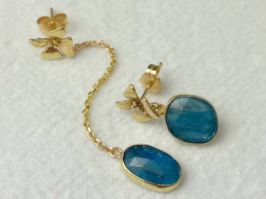 Asymmetrical 14k gold kyanite earrings with handcrafted flower detail and bezel-set blue stones displayed on a white background.