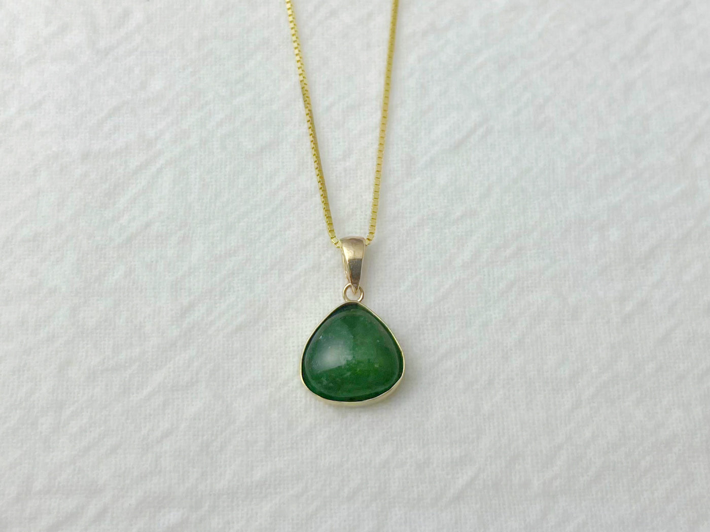Green teardrop pendant on a gold chain against a white background