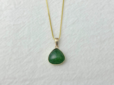 Green teardrop pendant on a gold chain against a white background