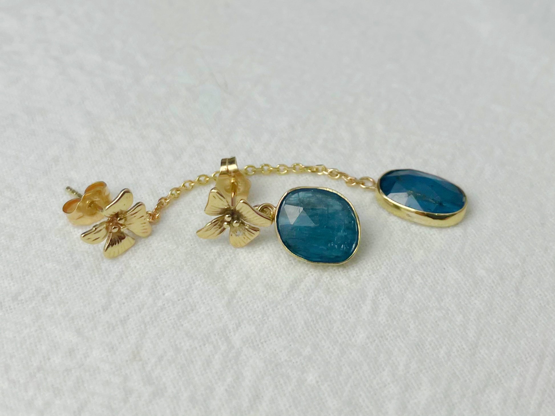 Detailed view of long 14k gold earring with flower stud, chain, and bezel-set oval kyanite drop.