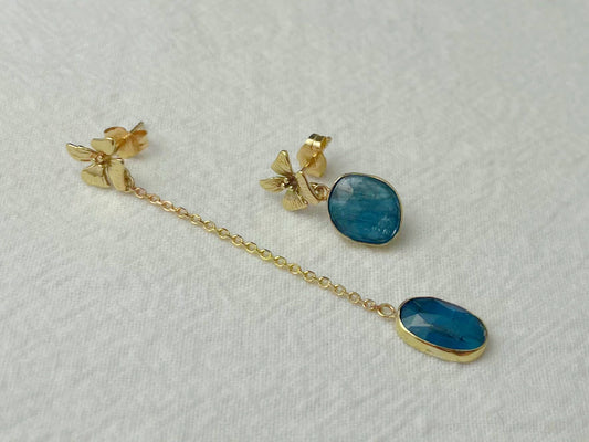 Close-up of asymmetrical gold earrings with blue kyanite stones and delicate flower accents shown worn.