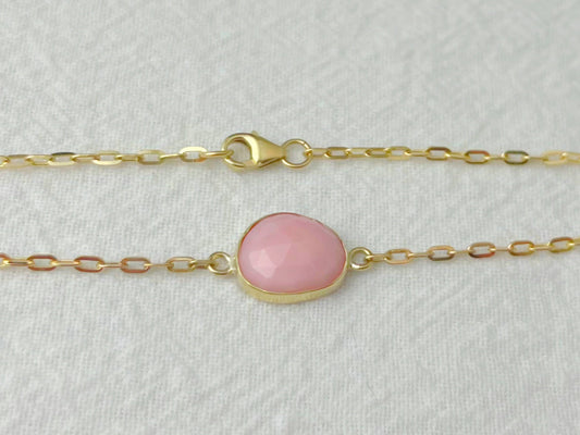 Gold bracelet with a pink gemstone on a light gray background