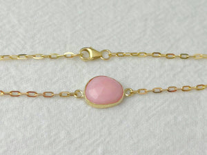 Gold bracelet with a pink gemstone on a light gray background