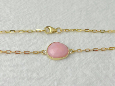 Gold bracelet with a pink gemstone on a light gray background
