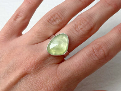 Hand wearing a ring with a green gemstone on a plain background