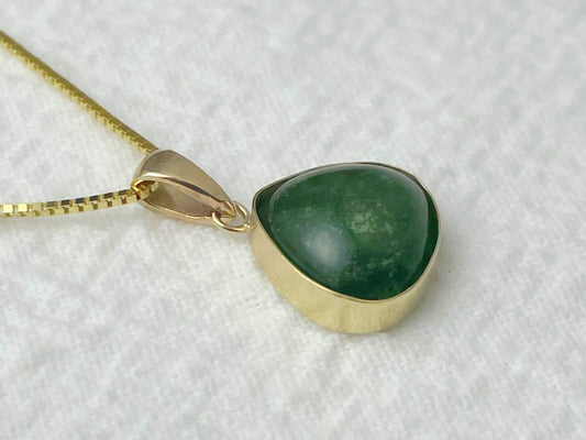 Close-up of a 14k gold pendant with a green tourmaline cabochon on a white background