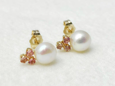 Pair of pearl earrings with gold and gemstone accents on a light background