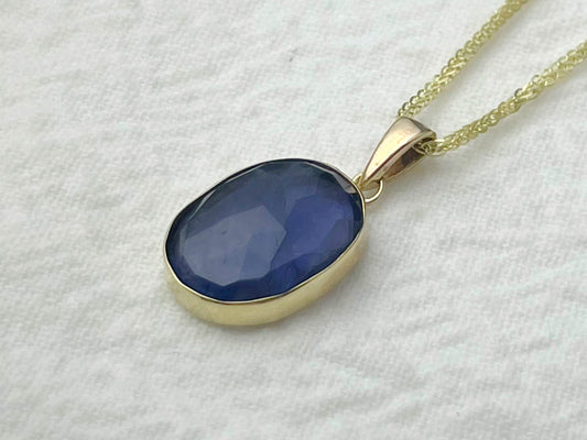 Gold necklace with a blue pendant on a white fabric background