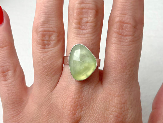 Hand wearing a ring with a green gemstone on a white background