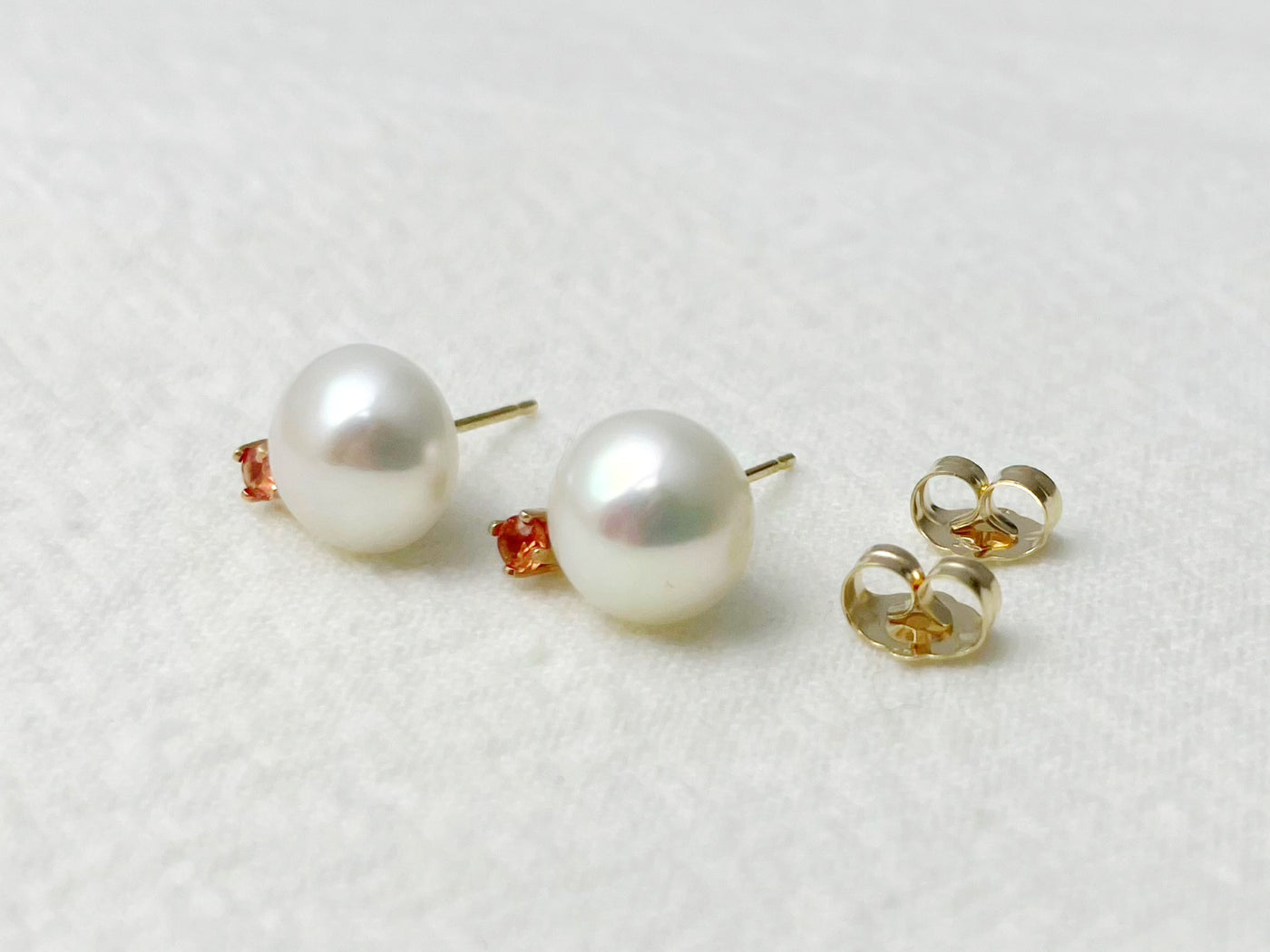 Pearl earrings with gold and orange accents on a white background