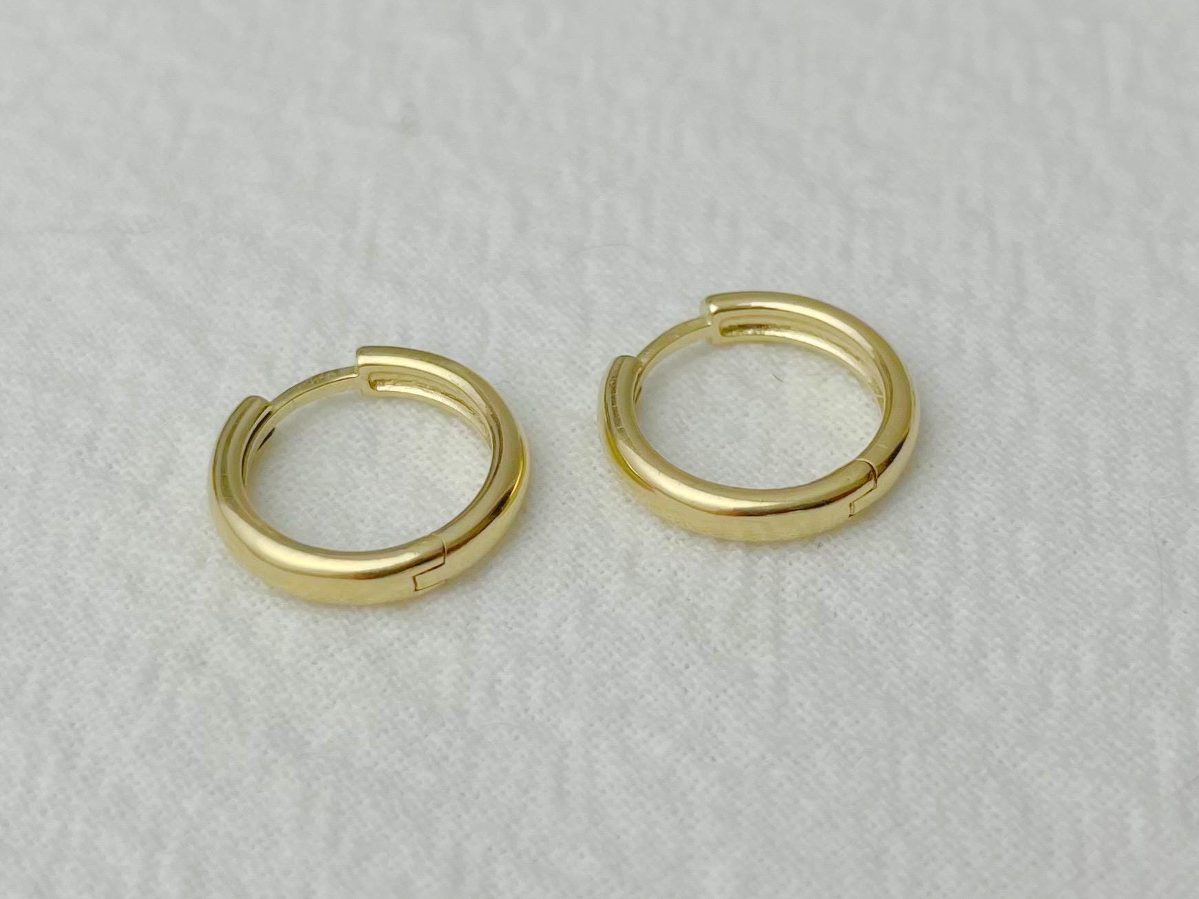 Petite yellow gold hoops reflecting soft light, photographed flat on a white cloth
