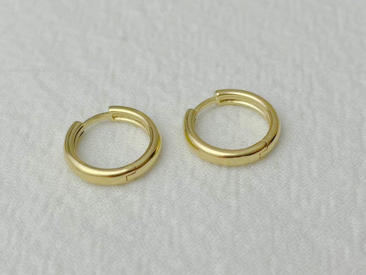 Petite yellow gold hoops reflecting soft light, photographed flat on a white cloth