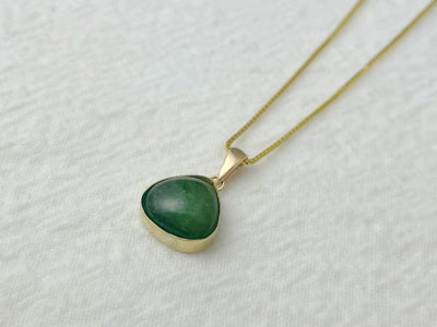 14k gold green tourmaline pendant lying with chain on a white surface