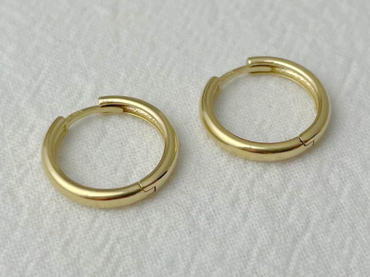 Close-up of medium-sized gold hoop earrings with hinged closure and smooth, rounded profile