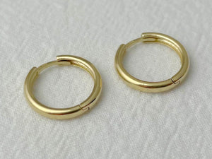 Close-up of medium-sized gold hoop earrings with hinged closure and smooth, rounded profile