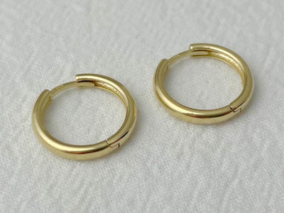 Close-up of medium-sized gold hoop earrings with hinged closure and smooth, rounded profile
