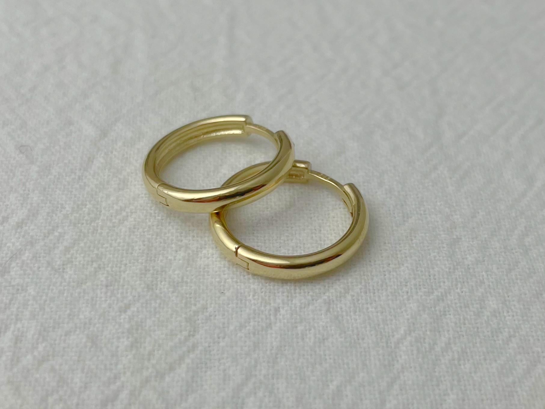 Pair of 14k yellow gold huggie hoop earrings with a polished finish, displayed on soft white fabric