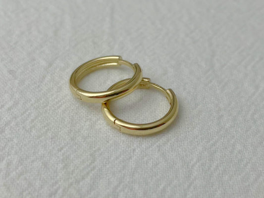 Pair of 14k yellow gold huggie hoop earrings with a polished finish, displayed on soft white fabric