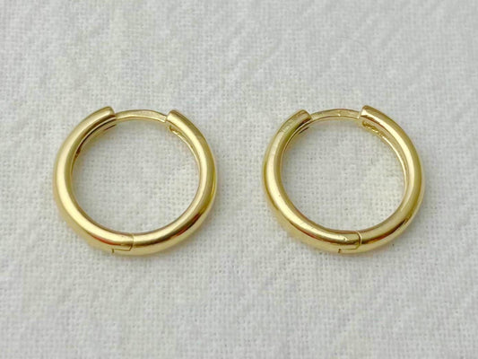 Pair of 13mm 14k yellow gold huggie hoop earrings with a high-polish finish on white fabric