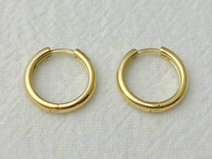 Pair of 13mm 14k yellow gold huggie hoop earrings with a high-polish finish on white fabric
