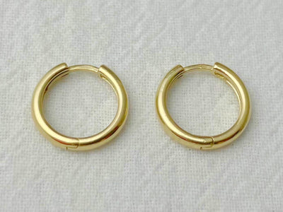 Pair of 13mm 14k yellow gold huggie hoop earrings with a high-polish finish on white fabric